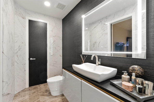 bathroom featuring vanity, toilet, and tile walls