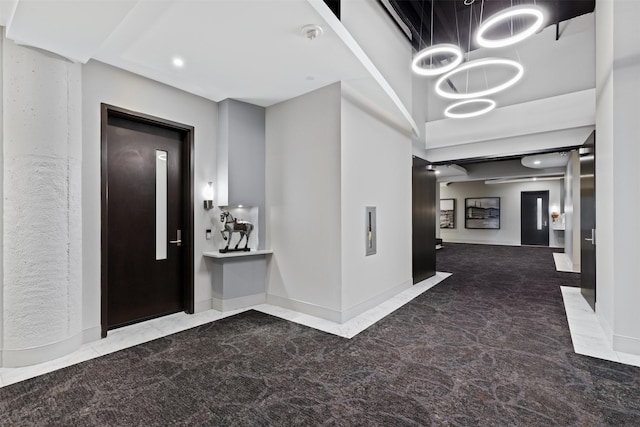 carpeted entryway featuring a notable chandelier, a towering ceiling, and elevator