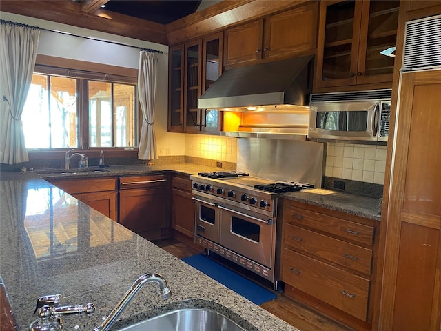 kitchen with sink, dark stone counters, stainless steel appliances, range hood, and backsplash