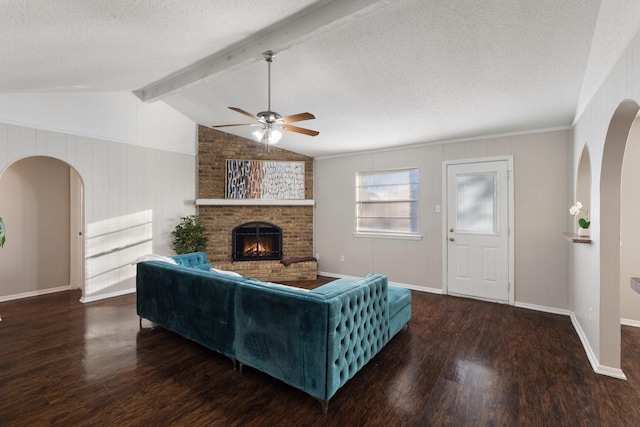 living room featuring a textured ceiling, ceiling fan, a fireplace, vaulted ceiling with beams, and dark hardwood / wood-style floors