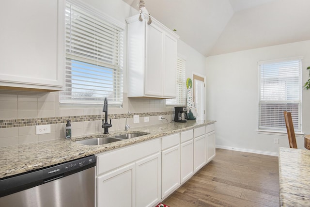 kitchen with light stone countertops, stainless steel dishwasher, vaulted ceiling, sink, and white cabinets