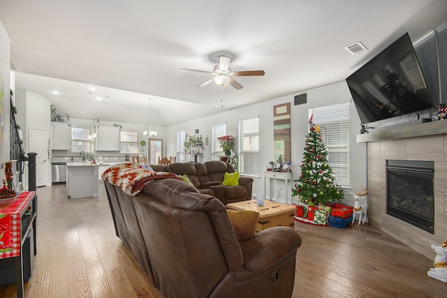 living room with a tile fireplace, lofted ceiling, light hardwood / wood-style floors, and ceiling fan with notable chandelier