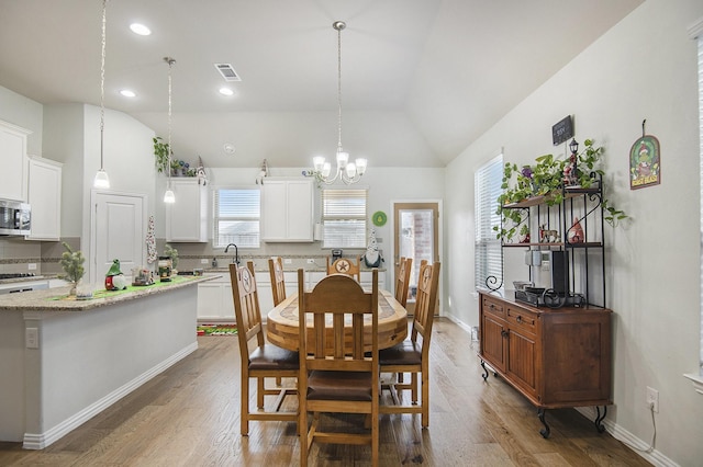 dining room with a chandelier, dark hardwood / wood-style floors, vaulted ceiling, and sink