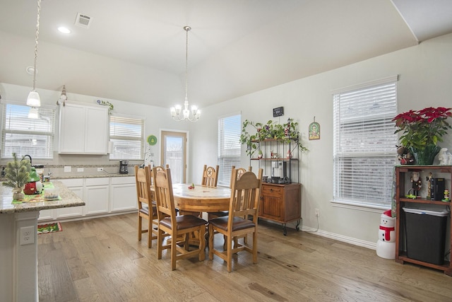 dining room with plenty of natural light, lofted ceiling, light wood-type flooring, and a chandelier