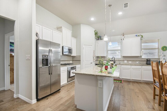 kitchen with pendant lighting, white cabinets, decorative backsplash, an island with sink, and appliances with stainless steel finishes