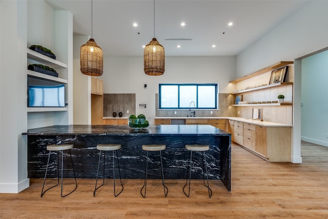 kitchen with backsplash, hanging light fixtures, a kitchen breakfast bar, light brown cabinetry, and light wood-type flooring