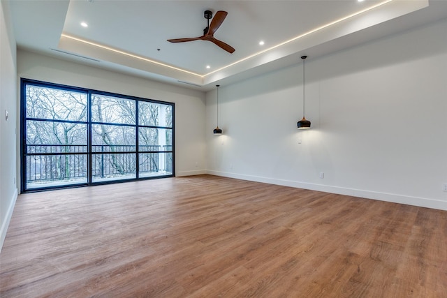 empty room with ceiling fan, wood-type flooring, and a tray ceiling