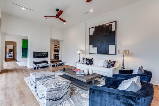 living room with light hardwood / wood-style floors, a large fireplace, and ceiling fan