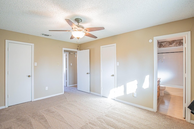 unfurnished bedroom with ensuite bath, ceiling fan, light carpet, and a textured ceiling