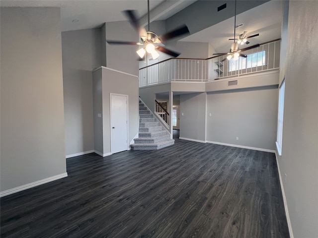 unfurnished living room featuring beam ceiling, ceiling fan, dark hardwood / wood-style flooring, and a high ceiling