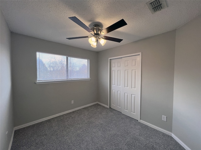 unfurnished bedroom featuring dark carpet, a textured ceiling, a closet, and ceiling fan