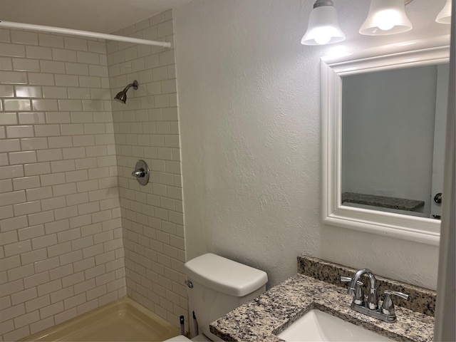 bathroom with tiled shower, vanity, and toilet