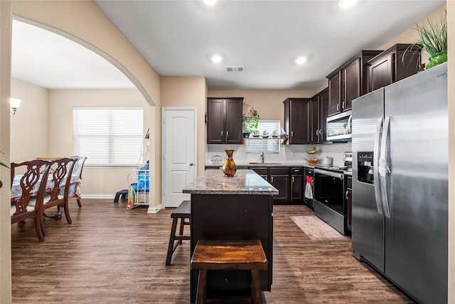 kitchen featuring sink, stainless steel appliances, light stone counters, a kitchen island, and dark hardwood / wood-style flooring