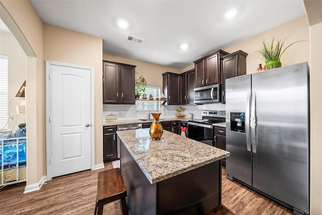 kitchen featuring dark brown cabinetry, light stone counters, a kitchen island, stainless steel appliances, and light hardwood / wood-style floors