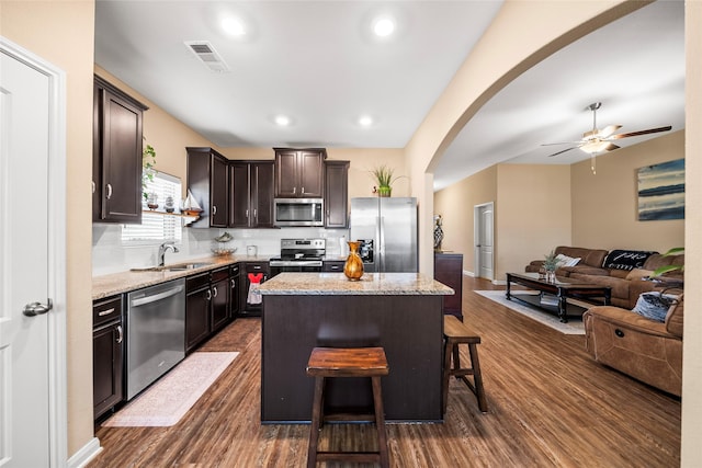 kitchen with a kitchen island, appliances with stainless steel finishes, sink, a kitchen breakfast bar, and light stone countertops