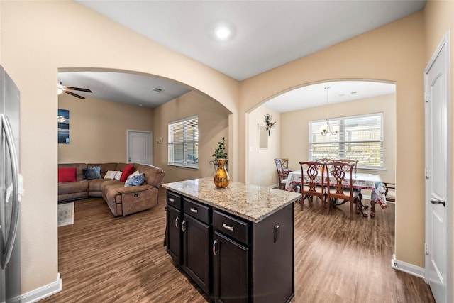 kitchen with a center island, light hardwood / wood-style flooring, pendant lighting, light stone countertops, and ceiling fan with notable chandelier