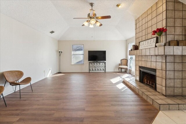 unfurnished living room featuring a tile fireplace, ceiling fan, wood-type flooring, and lofted ceiling