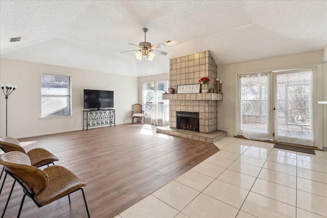 tiled living room featuring a textured ceiling, ceiling fan, a fireplace, and vaulted ceiling