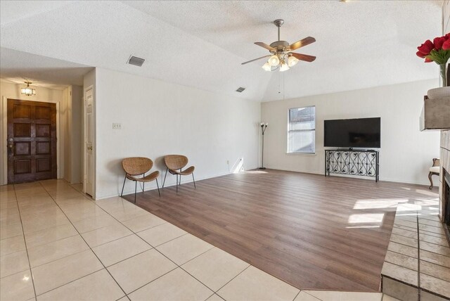 unfurnished living room with ceiling fan, light tile patterned flooring, lofted ceiling, and a textured ceiling