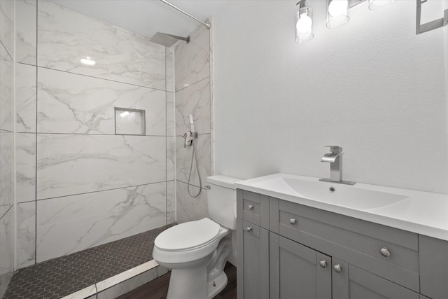 bathroom with hardwood / wood-style floors, vanity, toilet, and tiled shower