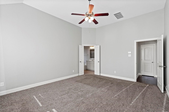 unfurnished bedroom featuring ensuite bath, ceiling fan, dark carpet, and vaulted ceiling