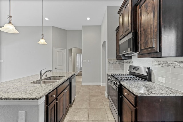 kitchen featuring sink, an island with sink, appliances with stainless steel finishes, decorative light fixtures, and dark brown cabinetry