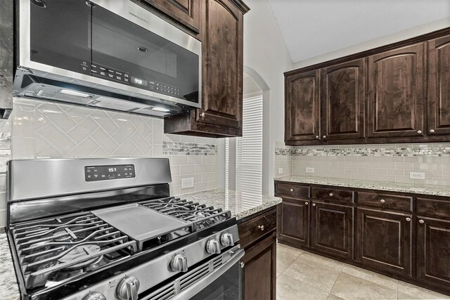 kitchen with lofted ceiling, decorative backsplash, light stone countertops, appliances with stainless steel finishes, and dark brown cabinets