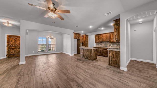 kitchen featuring backsplash, ceiling fan with notable chandelier, sink, hardwood / wood-style flooring, and a center island