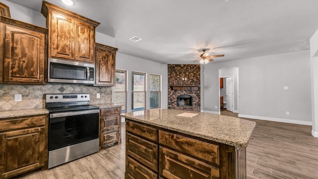 kitchen featuring light stone countertops, tasteful backsplash, a brick fireplace, stainless steel appliances, and a kitchen island