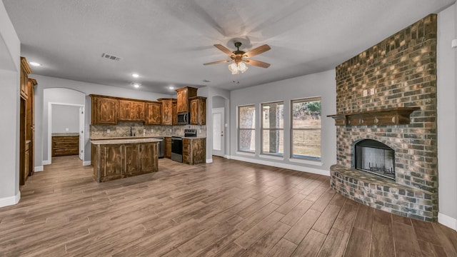 kitchen with a center island, decorative backsplash, a fireplace, wood-type flooring, and stainless steel appliances