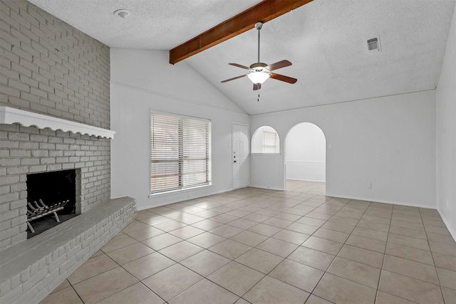 unfurnished living room featuring ceiling fan, vaulted ceiling with beams, a textured ceiling, a fireplace, and light tile patterned flooring