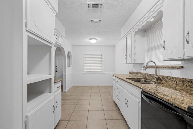 kitchen featuring stainless steel dishwasher, sink, light tile patterned floors, dark stone countertops, and white cabinets