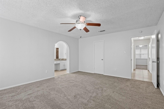 unfurnished bedroom featuring light carpet, ensuite bathroom, ceiling fan, a textured ceiling, and a closet