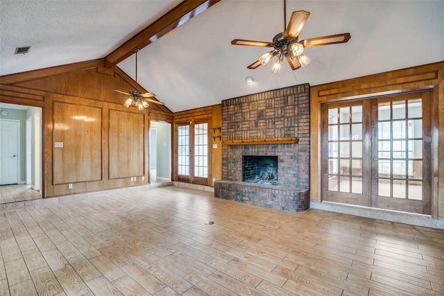 unfurnished living room with french doors, a brick fireplace, ceiling fan, wooden walls, and light hardwood / wood-style flooring