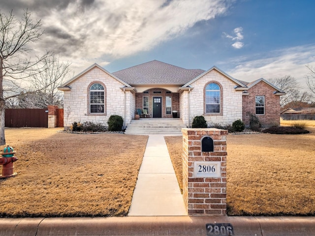 view of front facade featuring a shingled roof, fence, and brick siding