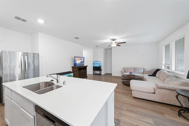 kitchen featuring sink, stainless steel appliances, an island with sink, white cabinets, and light wood-type flooring