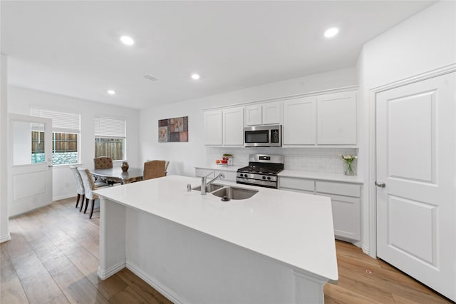 kitchen featuring a kitchen island with sink, white cabinets, sink, light wood-type flooring, and appliances with stainless steel finishes