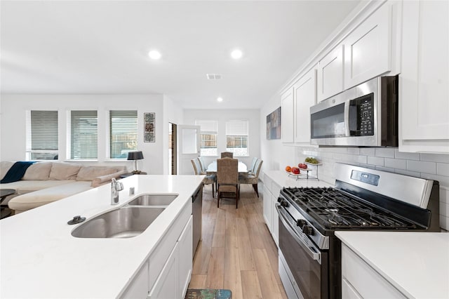 kitchen with sink, light hardwood / wood-style flooring, decorative backsplash, white cabinets, and appliances with stainless steel finishes