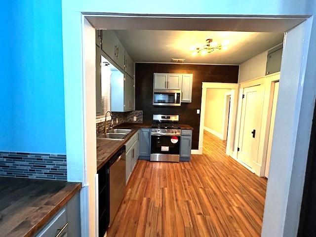 kitchen with backsplash, light hardwood / wood-style floors, stainless steel appliances, sink, and gray cabinets