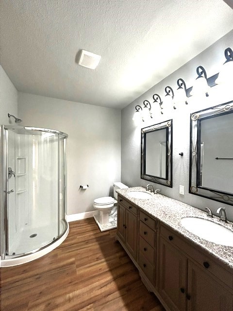 bathroom with a textured ceiling, toilet, vanity, a shower with shower door, and hardwood / wood-style flooring