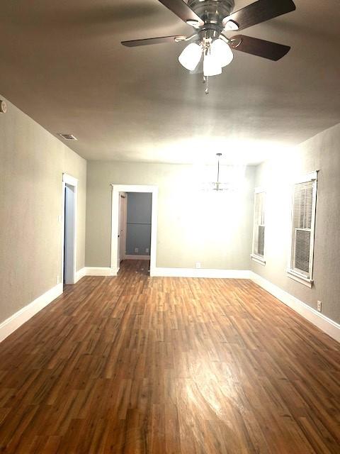 empty room with dark hardwood / wood-style floors and ceiling fan with notable chandelier