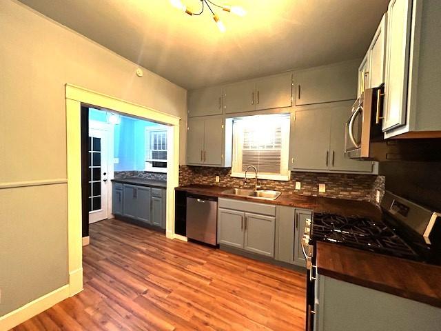 kitchen with light wood-type flooring, backsplash, gray cabinetry, stainless steel appliances, and sink