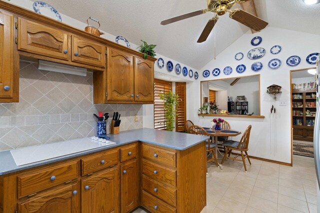 kitchen with lofted ceiling, light tile patterned floors, tasteful backsplash, stovetop, and kitchen peninsula