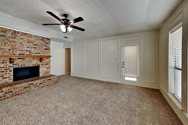 unfurnished living room with carpet flooring, a textured ceiling, a brick fireplace, and ceiling fan