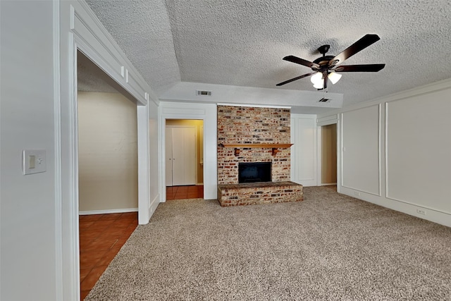 unfurnished living room featuring ceiling fan, carpet flooring, a textured ceiling, and a fireplace