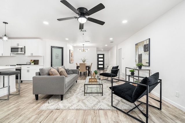 living room with ceiling fan with notable chandelier and light wood-type flooring