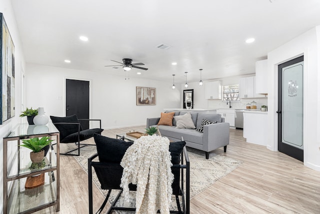 living room with ceiling fan, sink, and light wood-type flooring