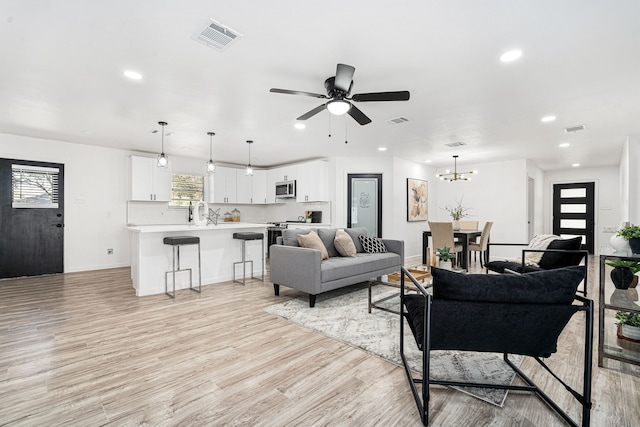 living room with ceiling fan with notable chandelier and light hardwood / wood-style flooring