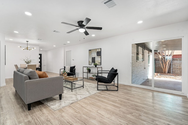 living room featuring ceiling fan with notable chandelier and light hardwood / wood-style floors