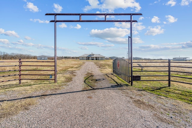 view of road with gravel driveway, a gate, a rural view, and a gated entry